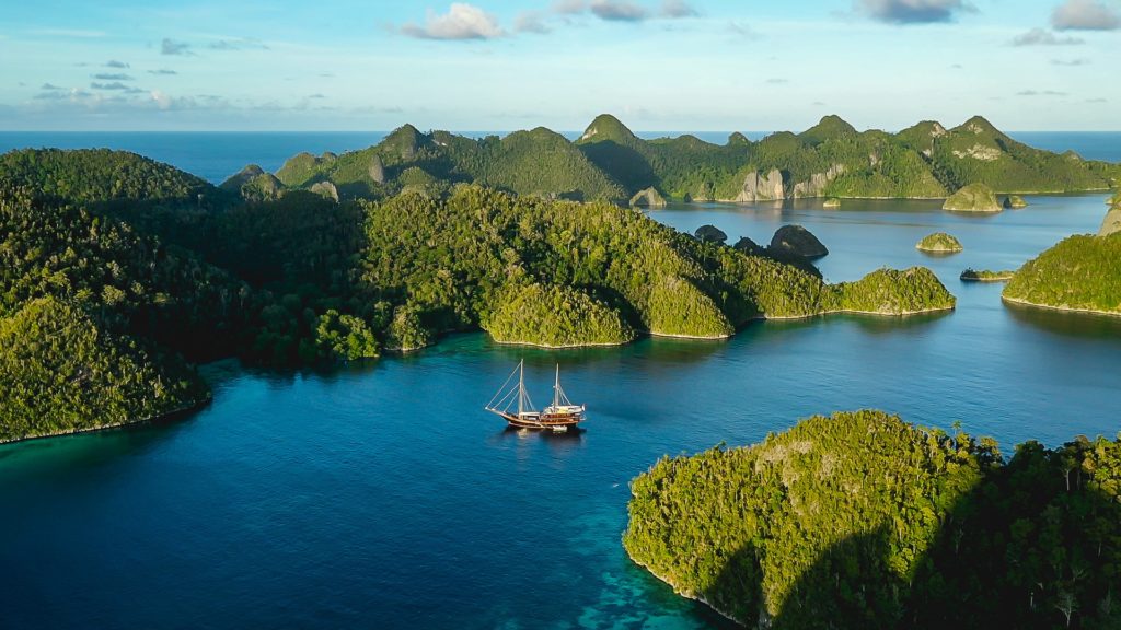 Aerial view of yacht on water amidst rainforest covered inlets and islands.