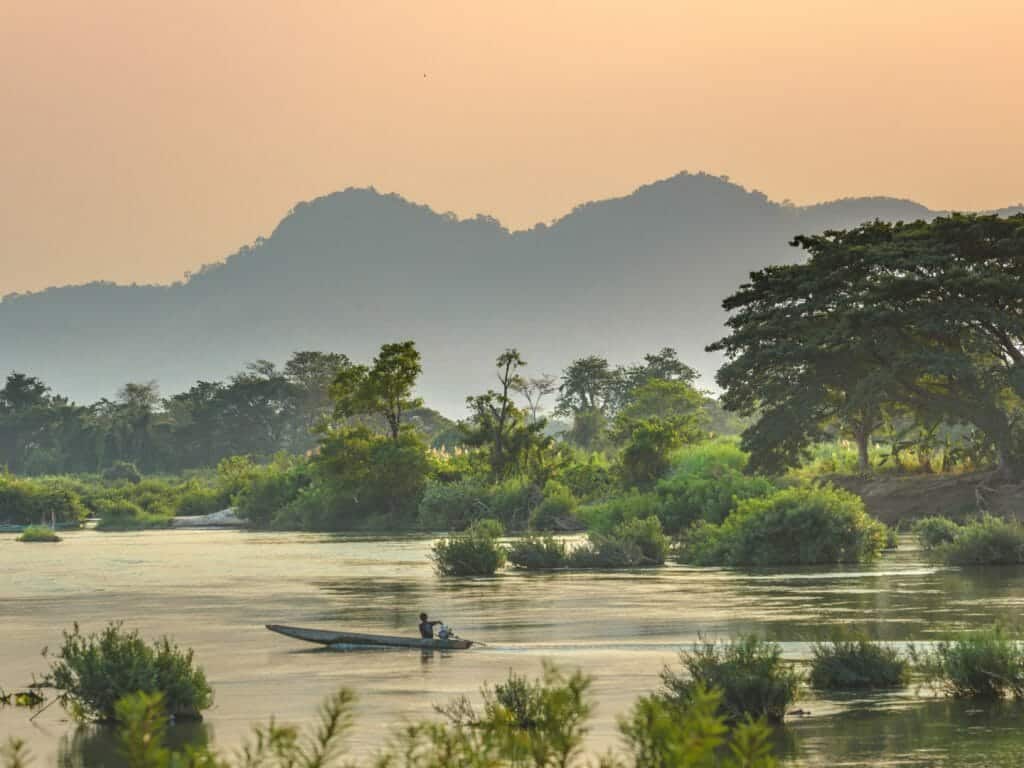 River view at sunrise with jungle covered banks and boat on river.