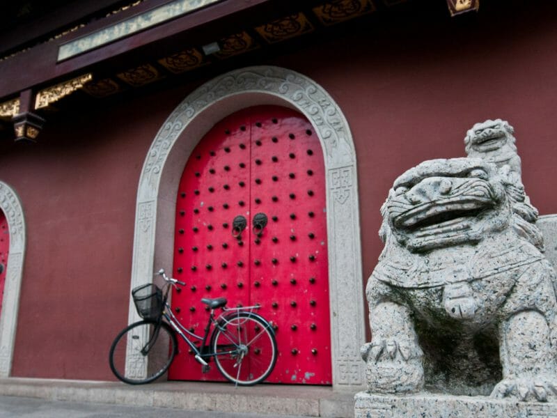 Red wall, red arched doors with bike against and stone carved lion in foreground.
