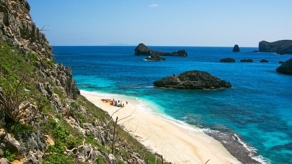 Clifftop view of beach with people and colourful kayaks on.