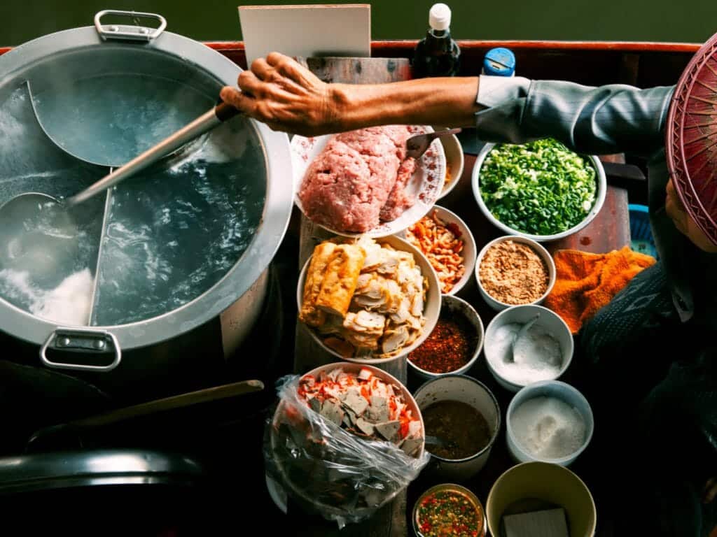 Aerial shot of a floating thai noodle maker on boat surrounded by steaming water and ingredients.