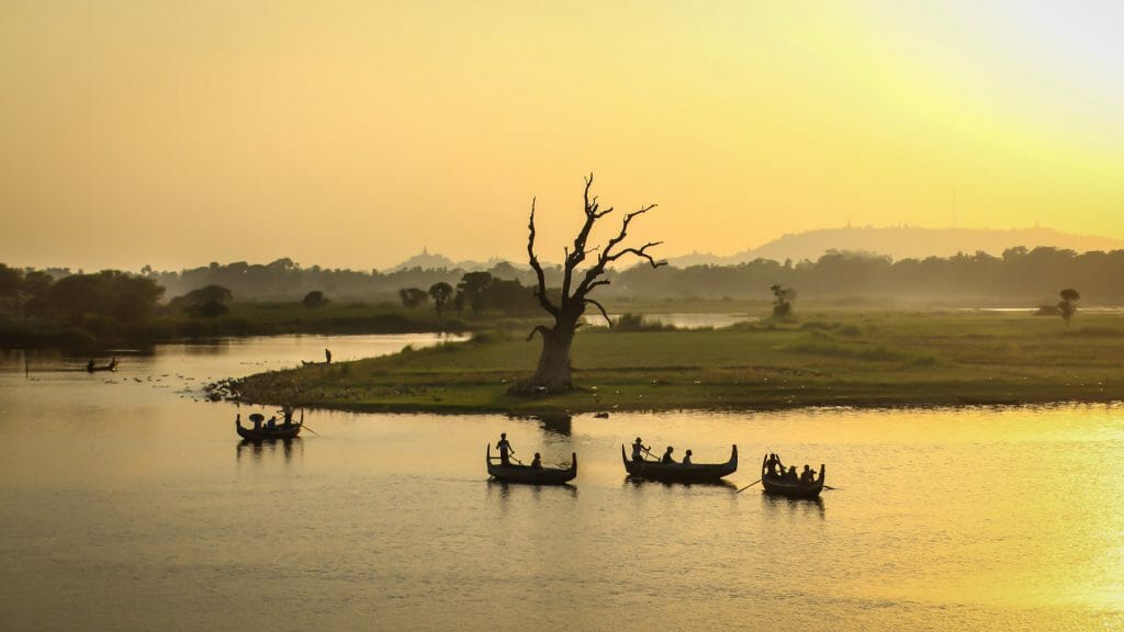 River at sunset with silhouettes of four traditional boats against yellow sky.