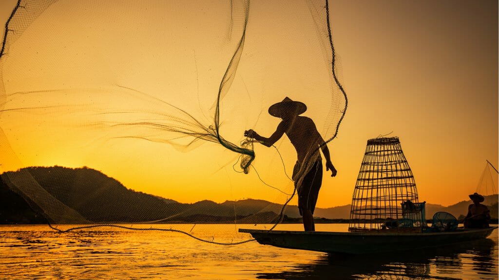 Fisherman silhouetted with his net being thrown as the sun sets