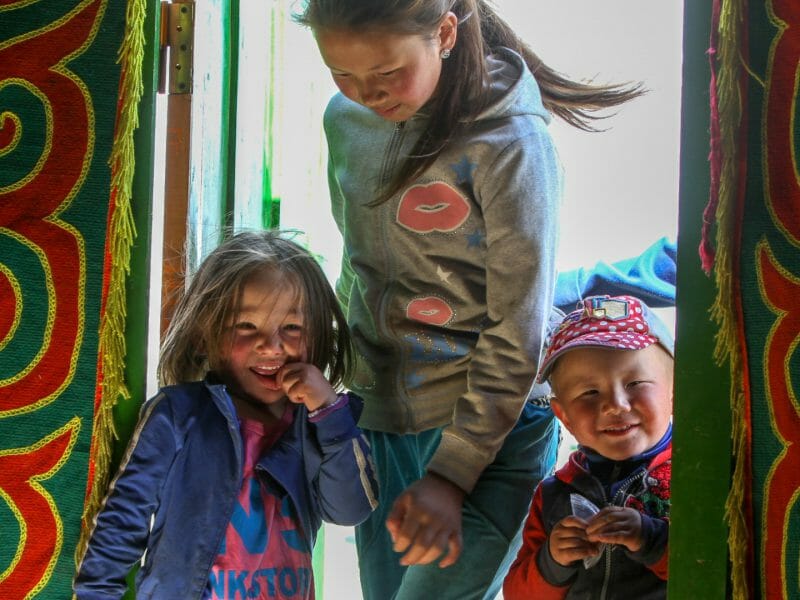 Three Mongolian children in brightly coloured ger doorway.