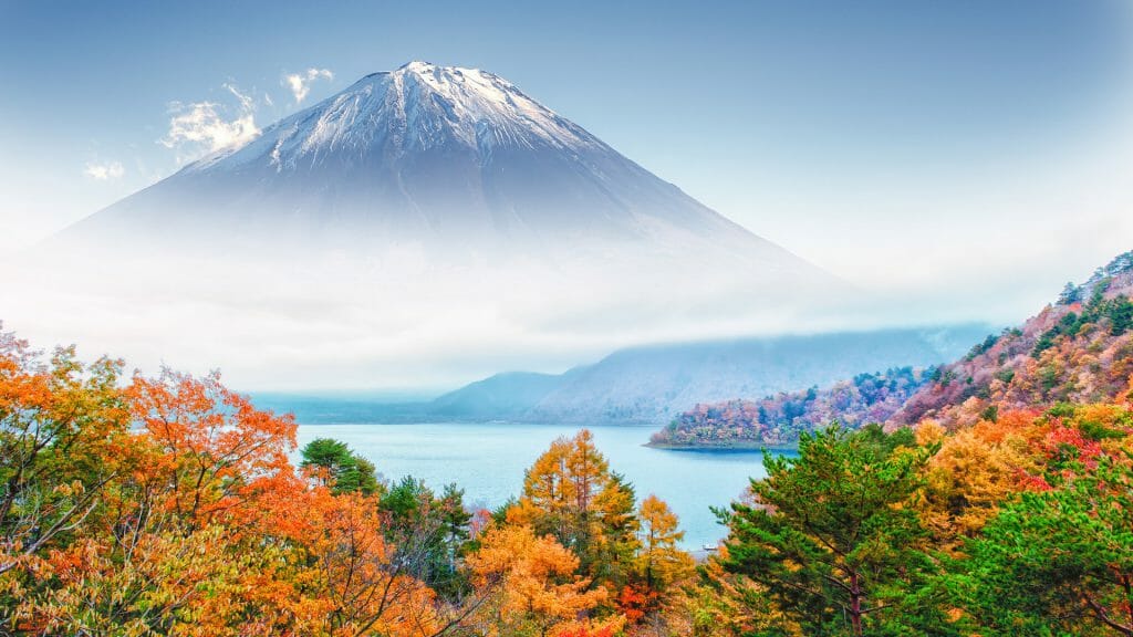 Autumnal foliage with lake and misty snow capped mount fuji beyond.