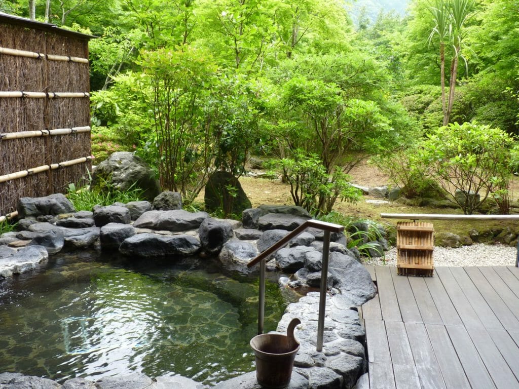 Private onsen in a ryokan in the Japanese Alps with a woodland garden beyond.