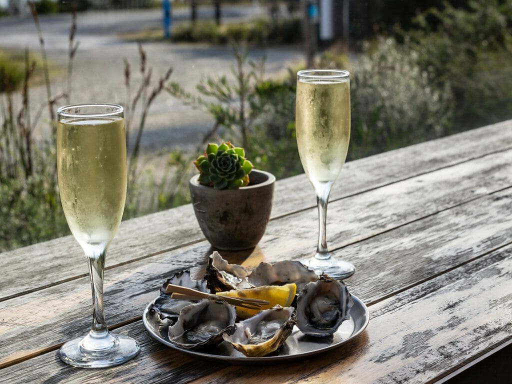 Two glasses of champagne and a plate of oysters on a wooden table.