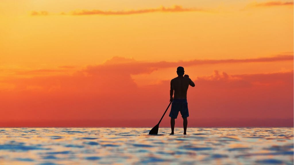 Lone paddle boarder silhouetted against the orange sky as the sunsets in Jimbaran Bay.