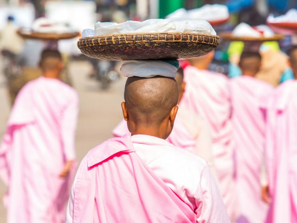 Rear view of pink robed nuns carrying goods on heads.