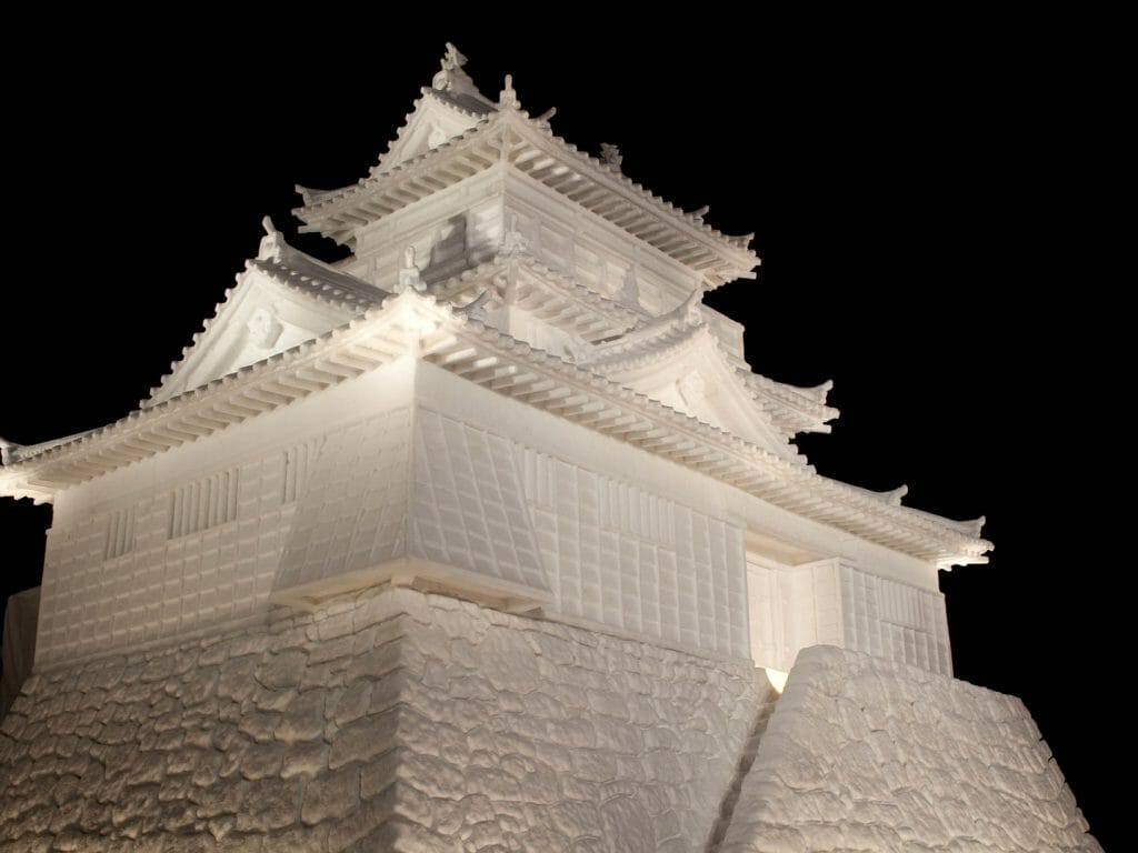 Snow sculpture of a traditional Japanese building against a black sky.