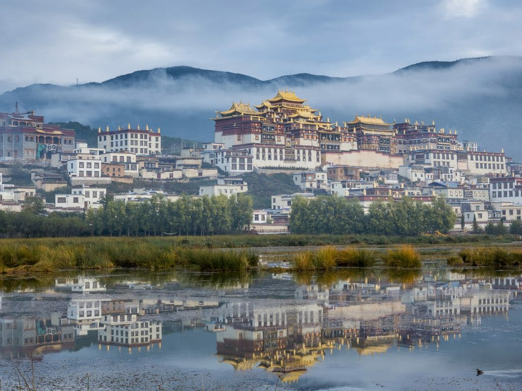 Tibetan Monastery town shrouded in low cloud, reflected in river.