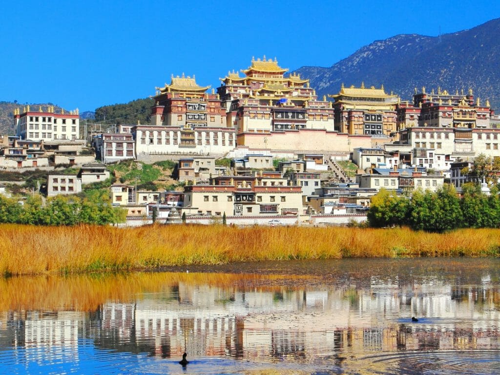 Tibetan Monastery town against blue sky, reflected in river.
