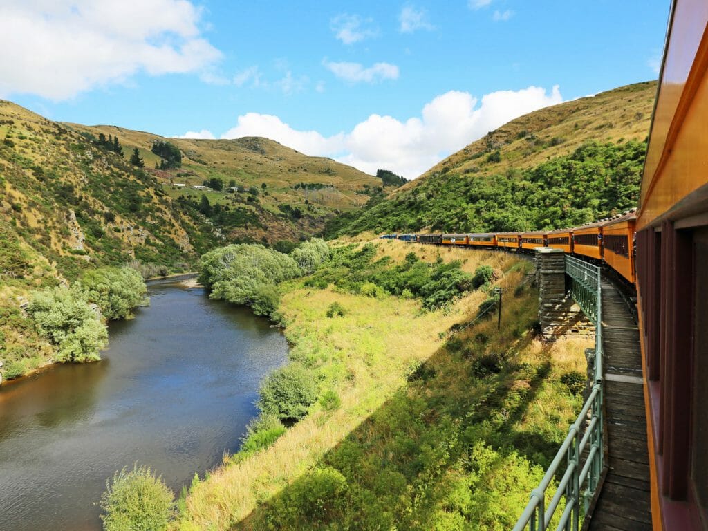 View from a train bending round a corner with river gorge on left and rolling green hills.