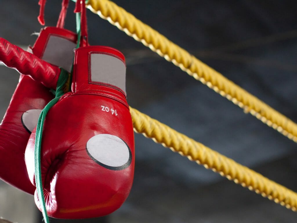 Yellow boxing ring ropes with pair of red muay thai boxing gloves hung on them.
