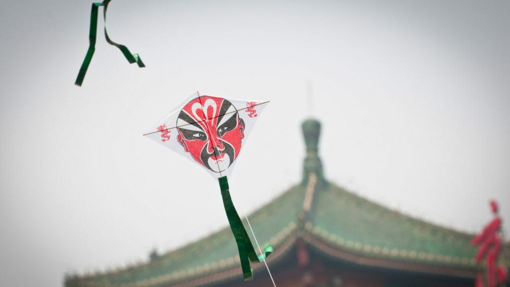 Traditional Chinese kite with Beijing opera face, Chinese rooftop in background.