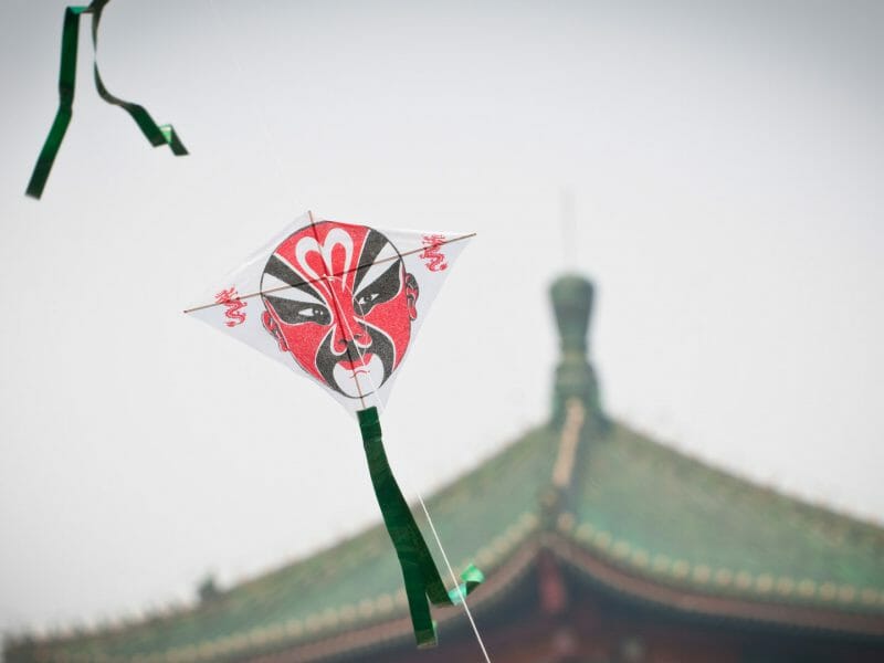 Traditional Chinese kite with Beijing opera face, Chinese rooftop in background.