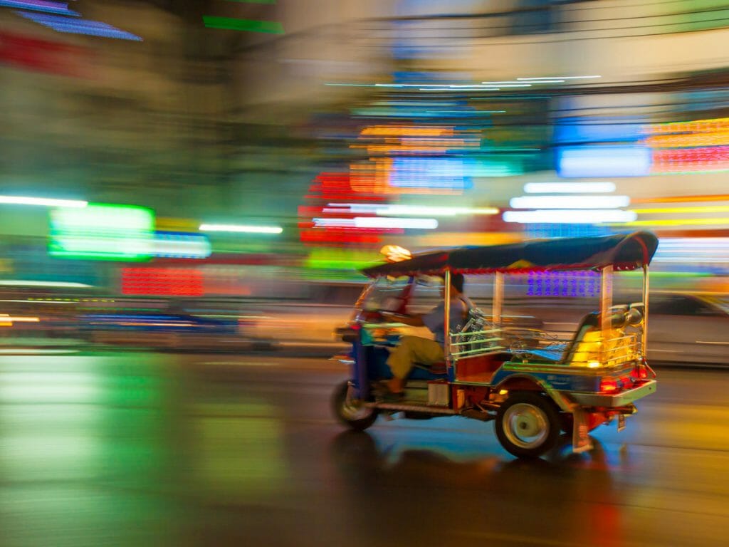 Blurry image of tuk tuk speeding through streets at night.