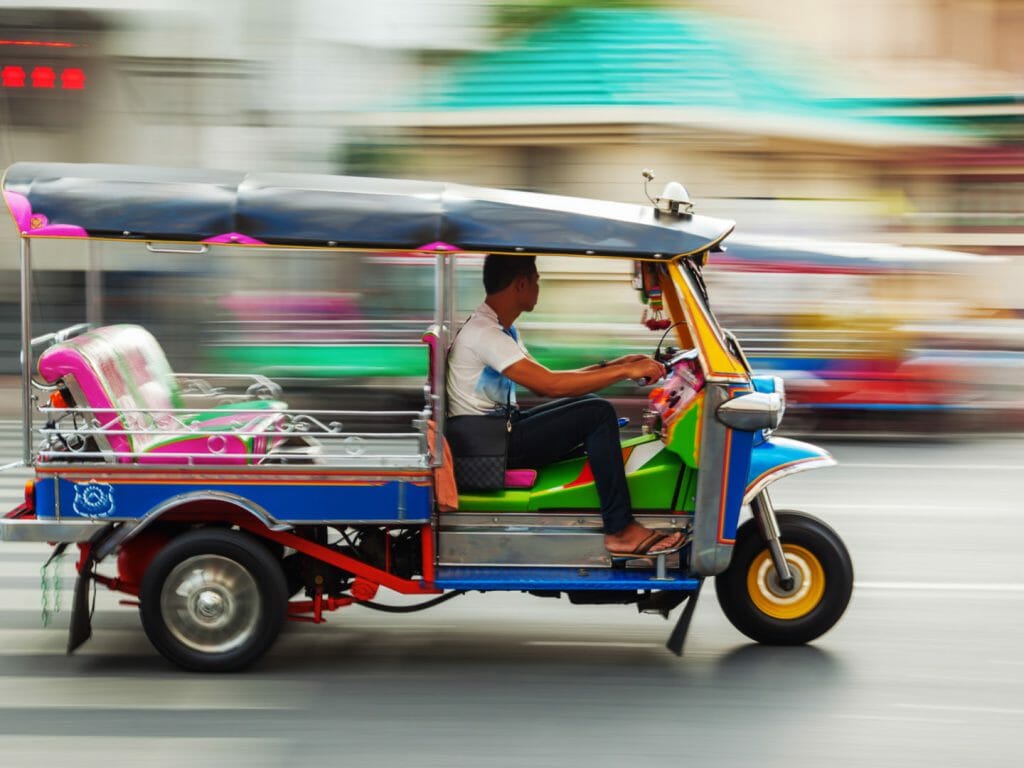 Tuk tuk in motion speeding through streets of Bangkok.