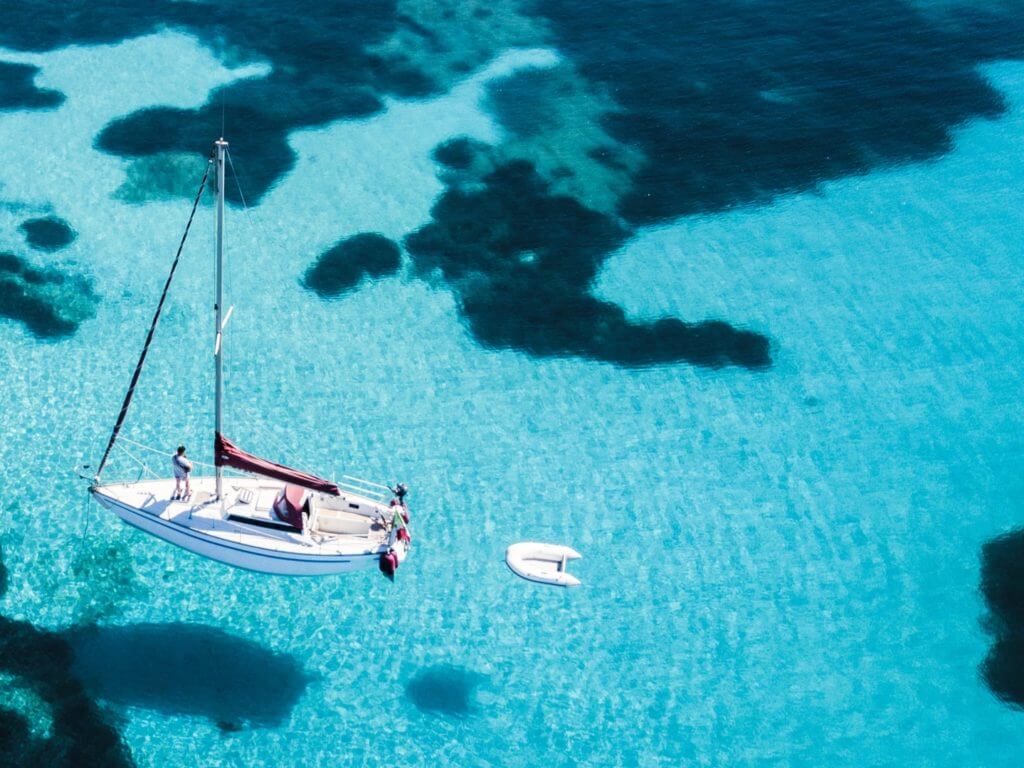 A white sail boat floats on amazing clear water off Sardinia's Emerald Coast in Italy