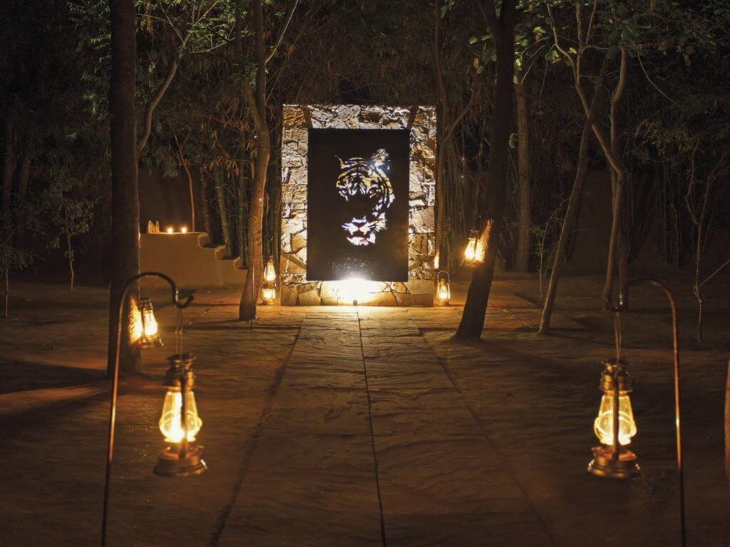 Pathway at night lit by hanging lanterns with lit tiger artwork at end of path.