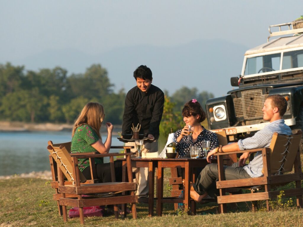 Guests sat enjoying sundowners on banks of river, Tiger Tops Karnali, Bardia National Park, Nepal