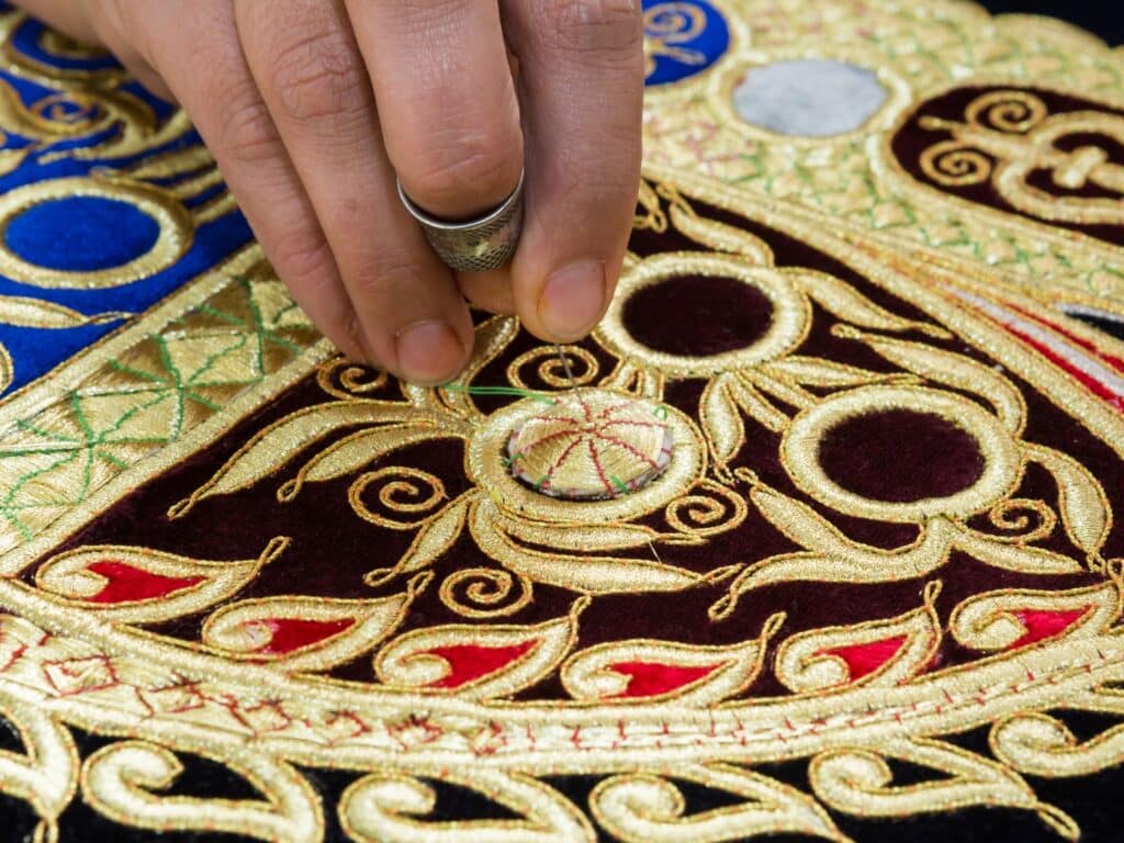 Close up of womans hand embroidering with gold silk.
