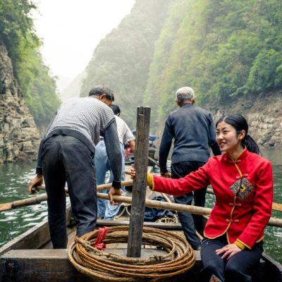 View from passenger onboard a traditional Chinese rowing boat with men stood rowing through narrow river gorge.