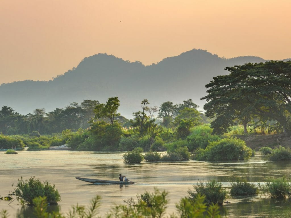 River view at sunrise with jungle covered banks and boat on river.