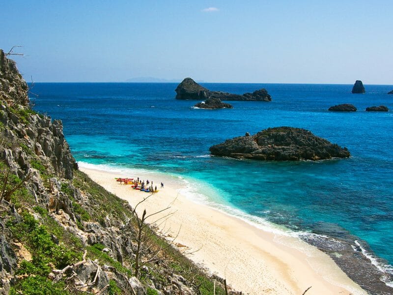 Clifftop view of beach with people and colourful kayaks on.