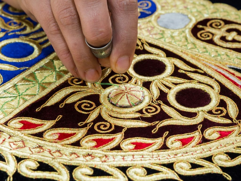 Close up of woman's hand embroidering with gold silk.