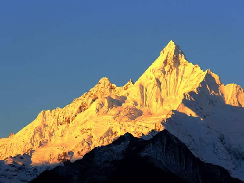 Snow covered peak of jagged mountain against bright blue sky.