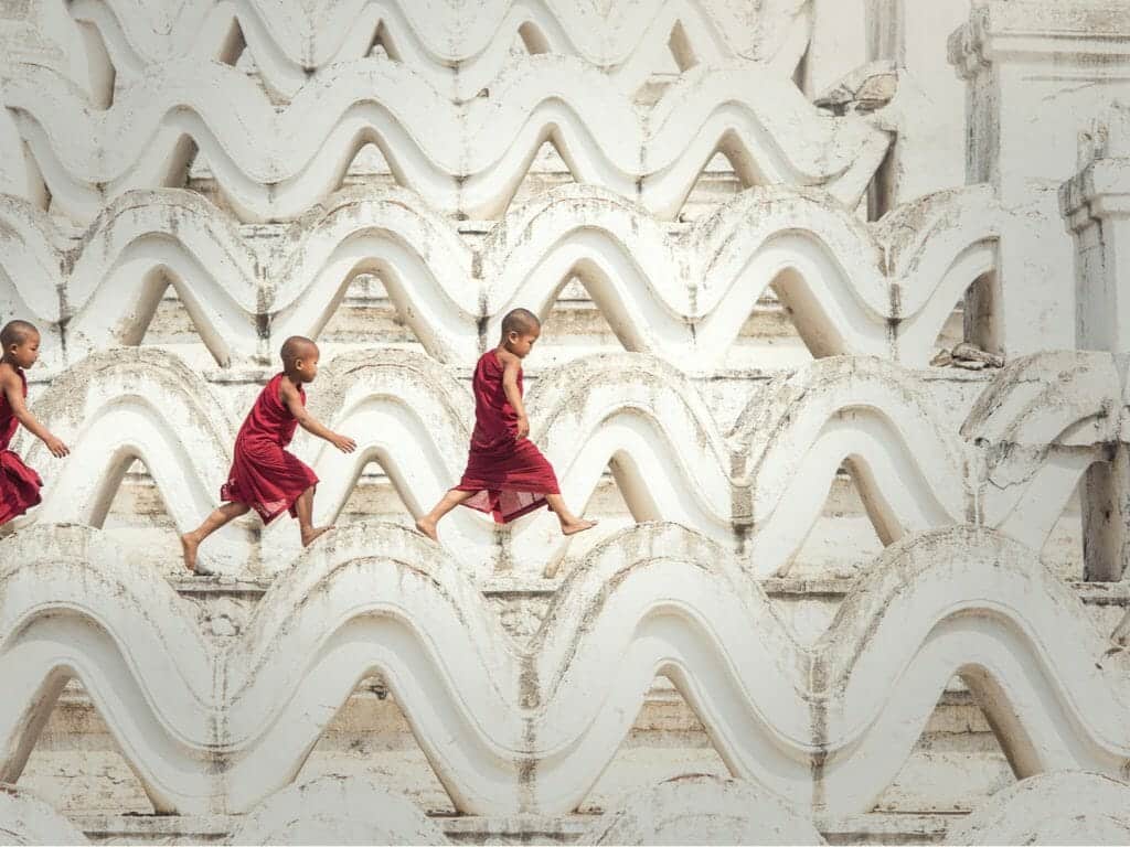 Three Saffron robed novice monks walking on white wave shaped carvings of temple.