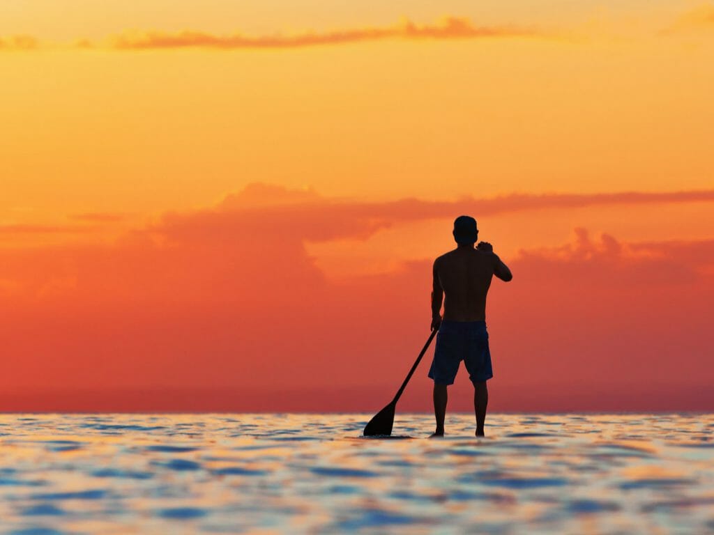 Lone paddle boarder silhouetted against the orange sky as the sunsets in Jimbaran Bay.