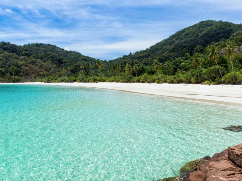 Turquoise clear water leading to white beach backed by tropical rainforest.
