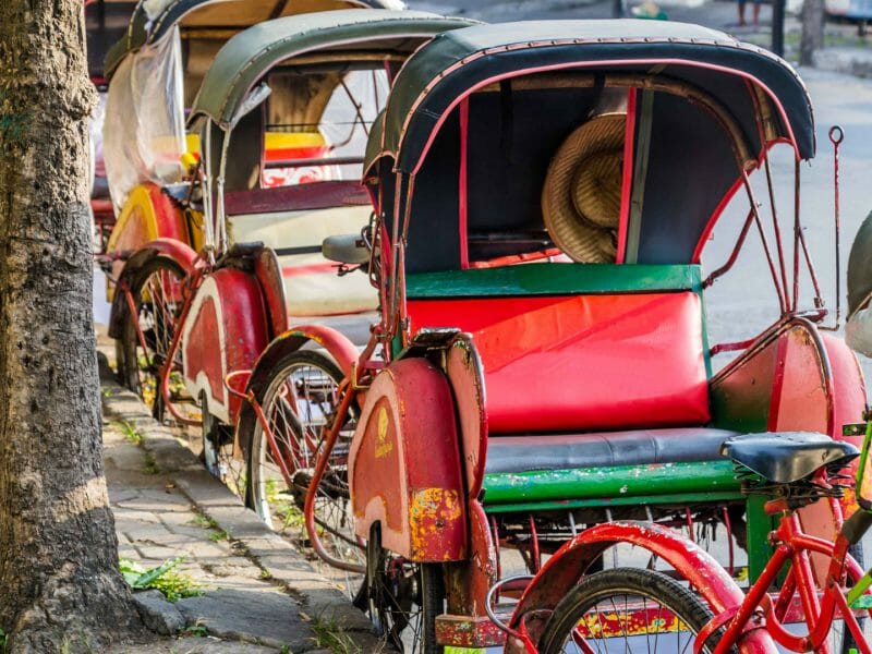 Traditional red and green rickshaws lined up along the kerbside.