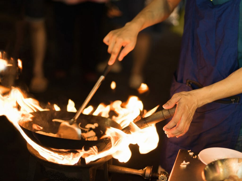 Close up of chef cooking on a flame surrounded wok.