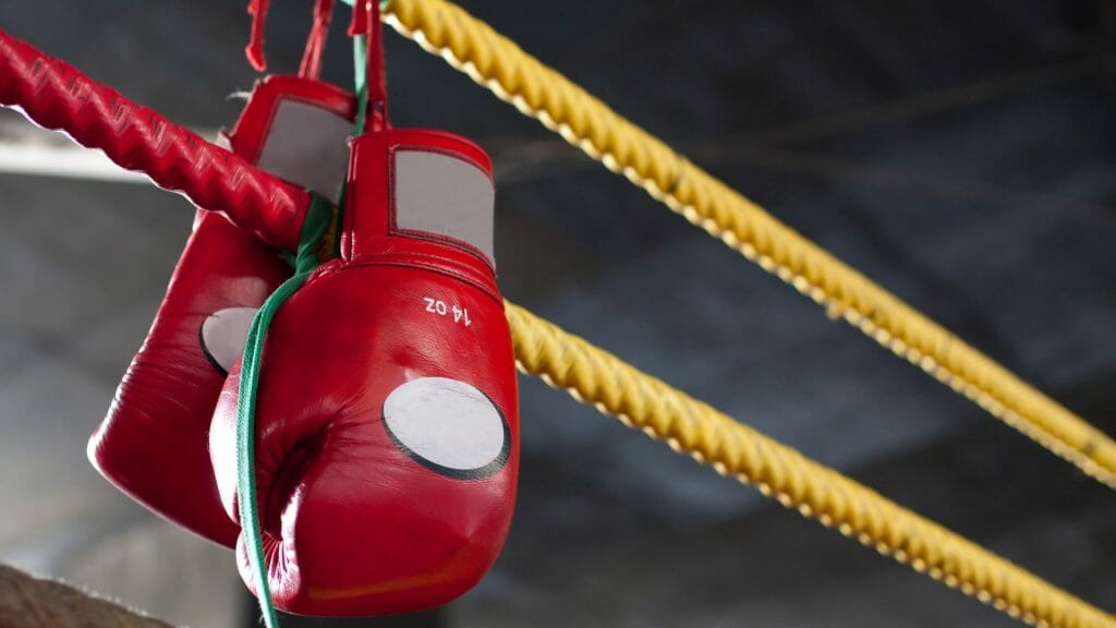 Yellow boxing ring ropes with pair of red muay thai boxing gloves hung on them.