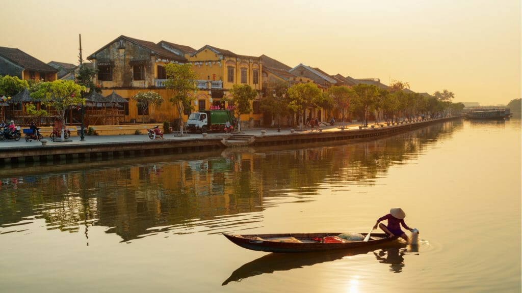 Vietnamese booking in a traditional wooden boat on the Thu Bon River in Hoi An at sunrise.