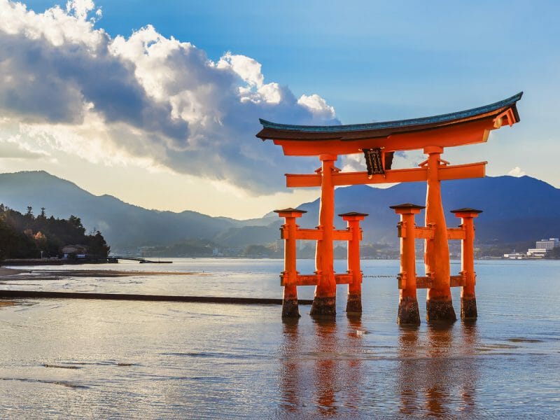 Traditional Japanese red gate in the ocean against a mountain backdrop.