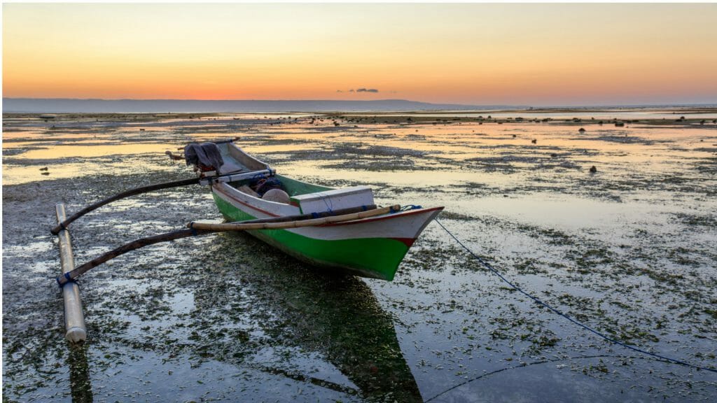 Traditional fishing boat on the shore at low tide as the sun sets.