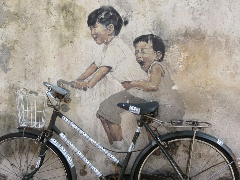 Bike leaning against wall with graffiti street art of two children sat on bike.