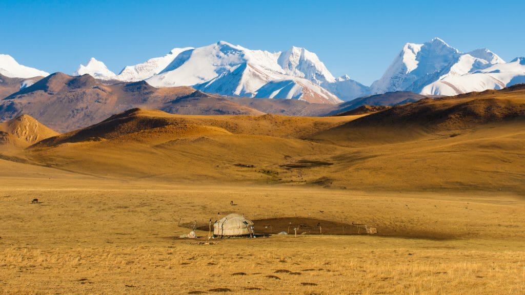Traditional yurt on open steppes with snow capped mountains in the background.