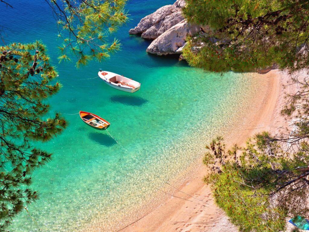Boats float on clear water off a hidden beach on the Makarska Riviera in Croatia