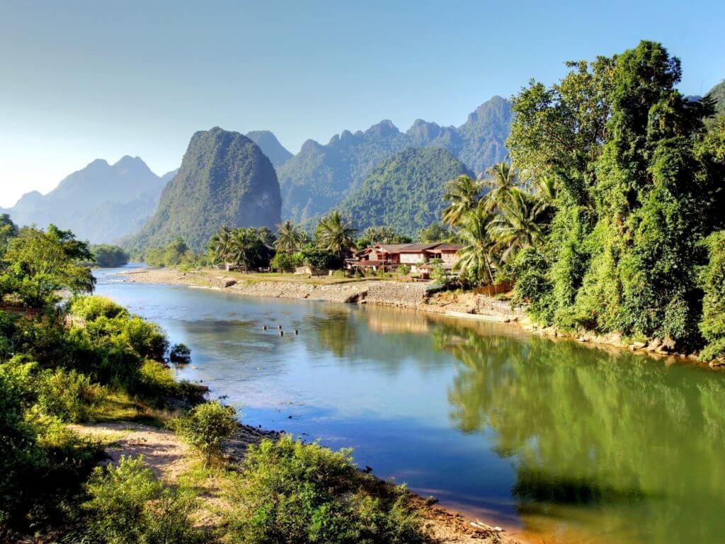 The Mekong River flanked by lush green trees with mountains in the background