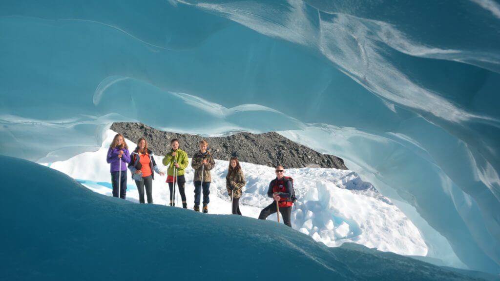 Vibrant blue ice with view through carved hole to six people standing on ice.