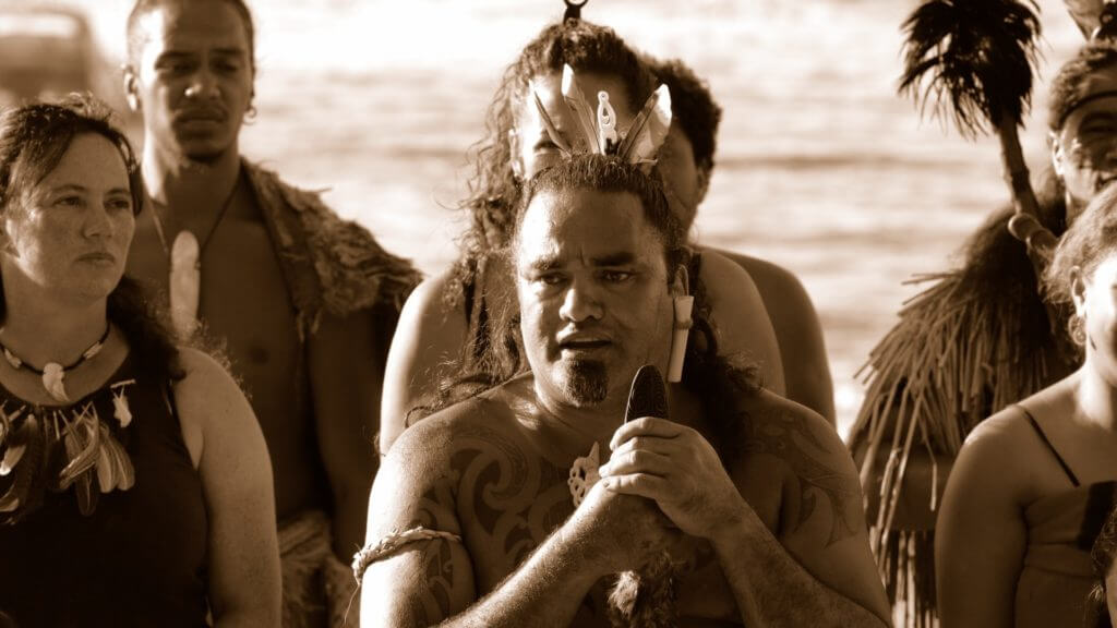 Black and white image of Maori people with tatoos, traditional jewellery and feathers in hair.