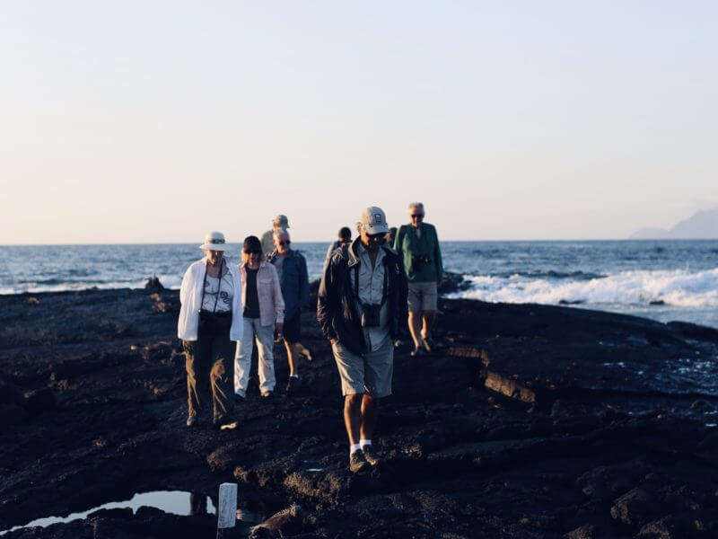 A group of tourists walk on a rocky peninsula with their naturalist guide in the Galapagos Islands