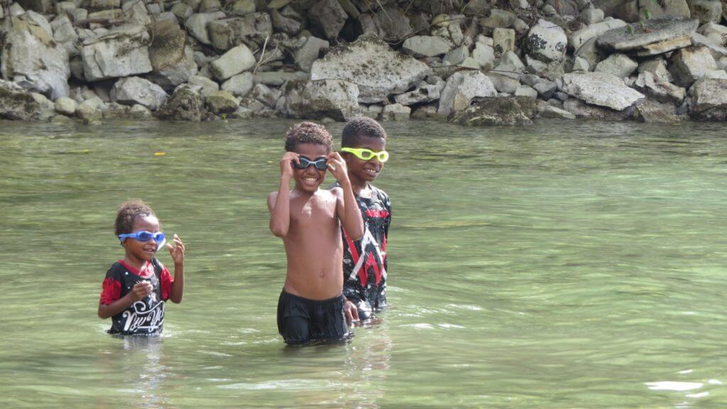 Three Indonesian village boys stook in water wearing newly gifted snorkels and big smiles.