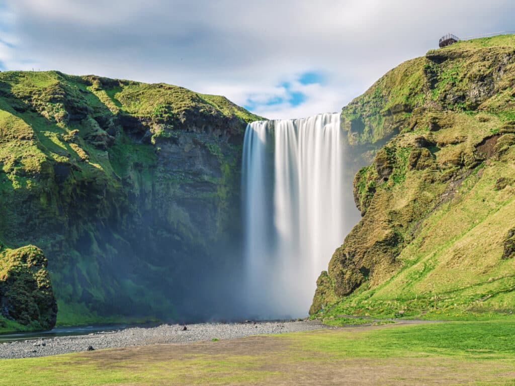 View of waterfall amid green hills, Iceland